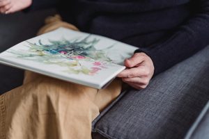 Person holding watercolor flower artwork while seated on couch